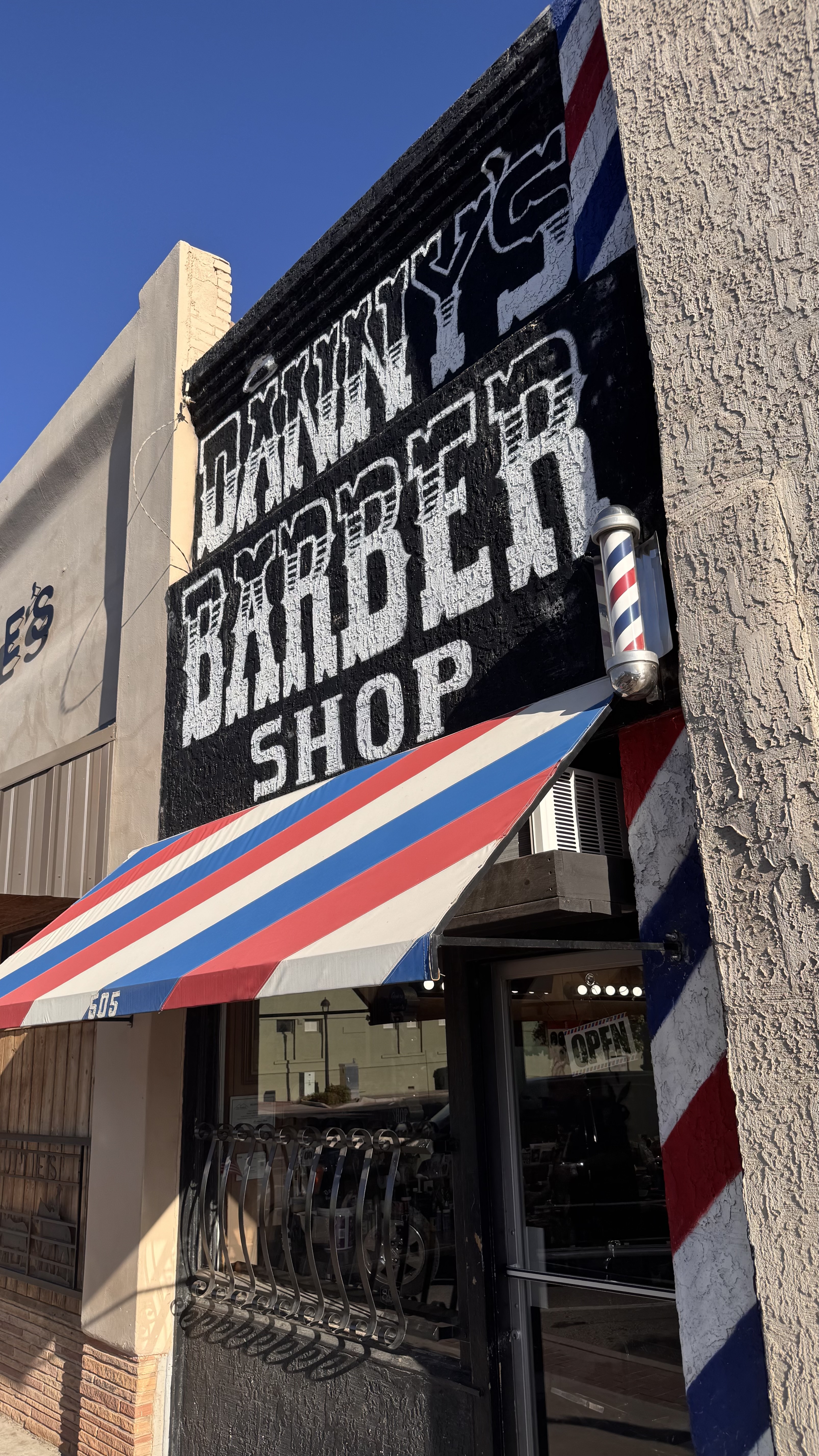 Front of Danny's Barber Shop with black painted sign and red, white, and blue awning